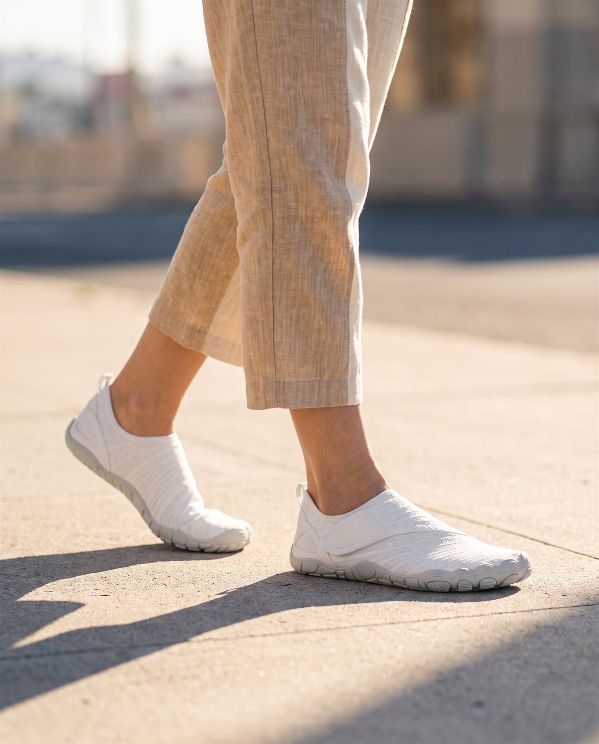 Close-up of a person walking on a sunlit pavement wearing white Brizway Flex shoes